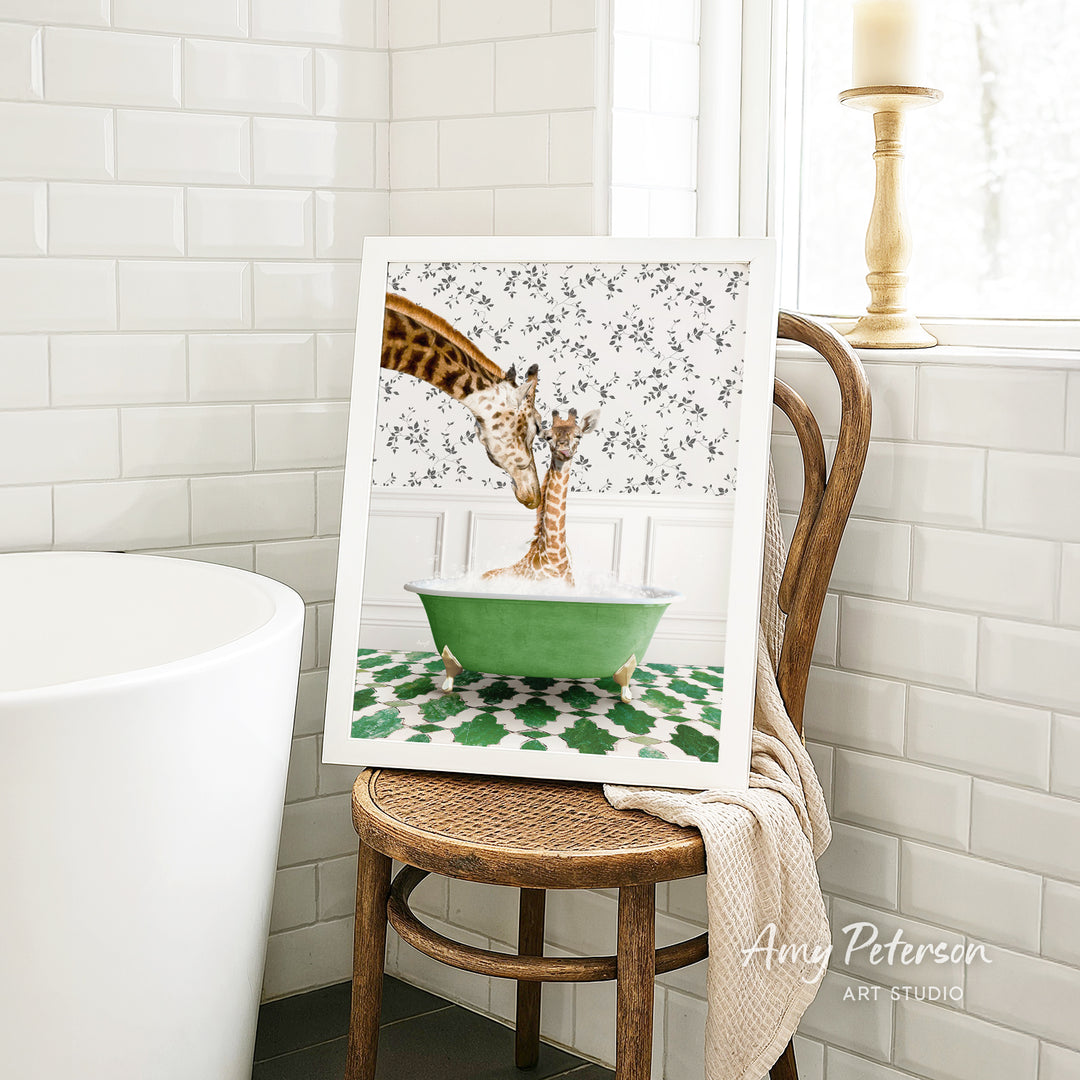 A framed image of two giraffes sitting in a green bathtub, surrounded by a floral pattern, is displayed on a wooden chair in a bathroom setting.