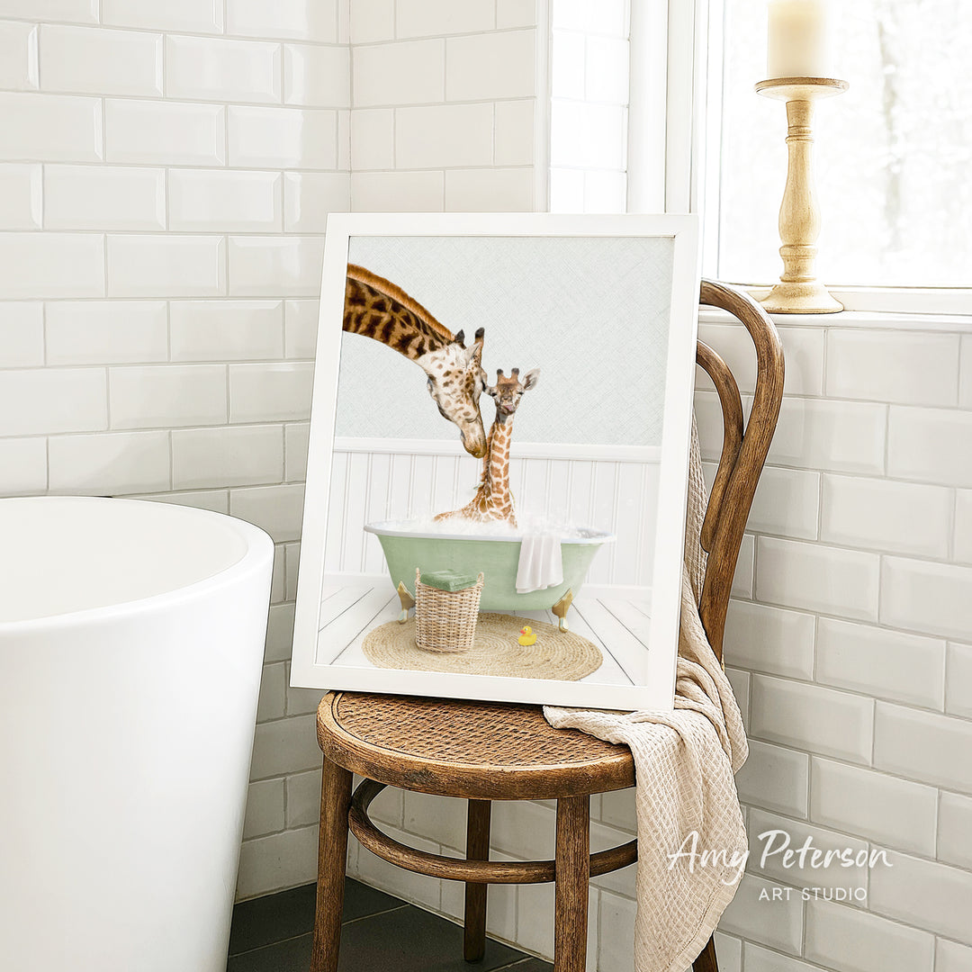 A framed image of two giraffes sitting in a bathtub, with one giraffe appearing to be bathing the other giraffe. The image is displayed on a wooden chair in a bathroom setting.