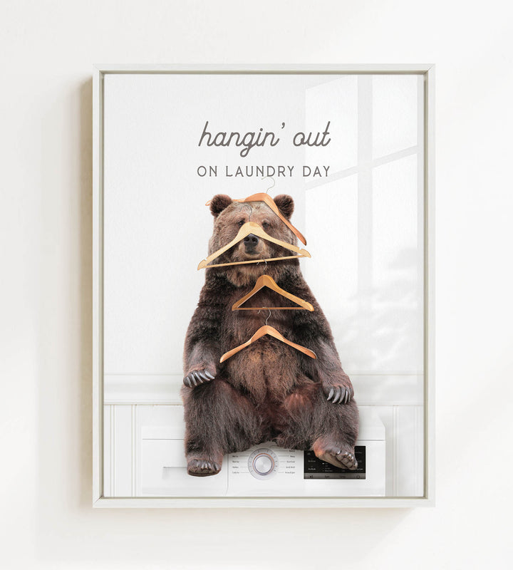 A brown bear sitting on a washing machine, surrounded by hanging clothes, with the text "hangin' out on laundry day" displayed above the bear.