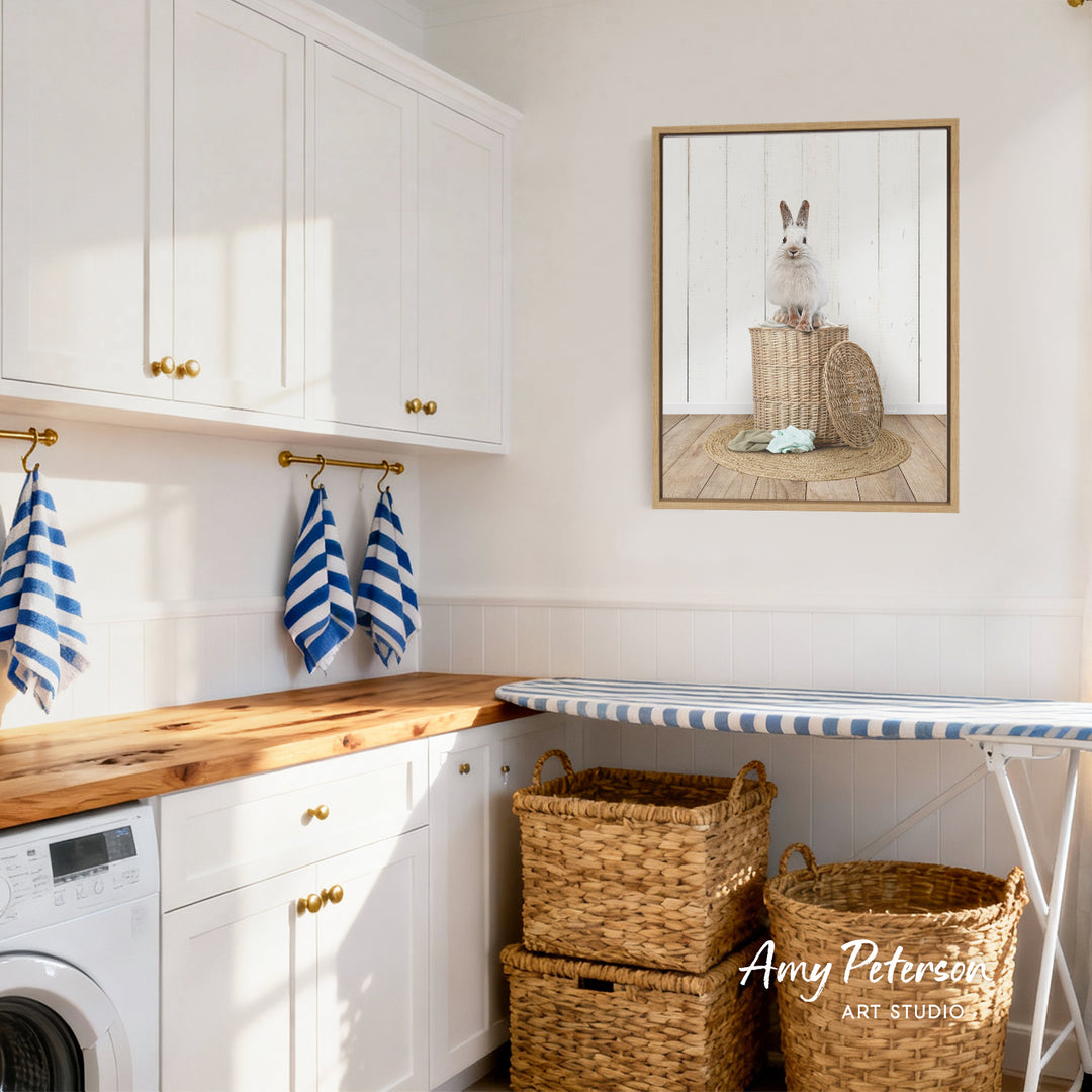 A cozy laundry room with white cabinets, a wooden countertop, and a framed picture of a rabbit on a basket.