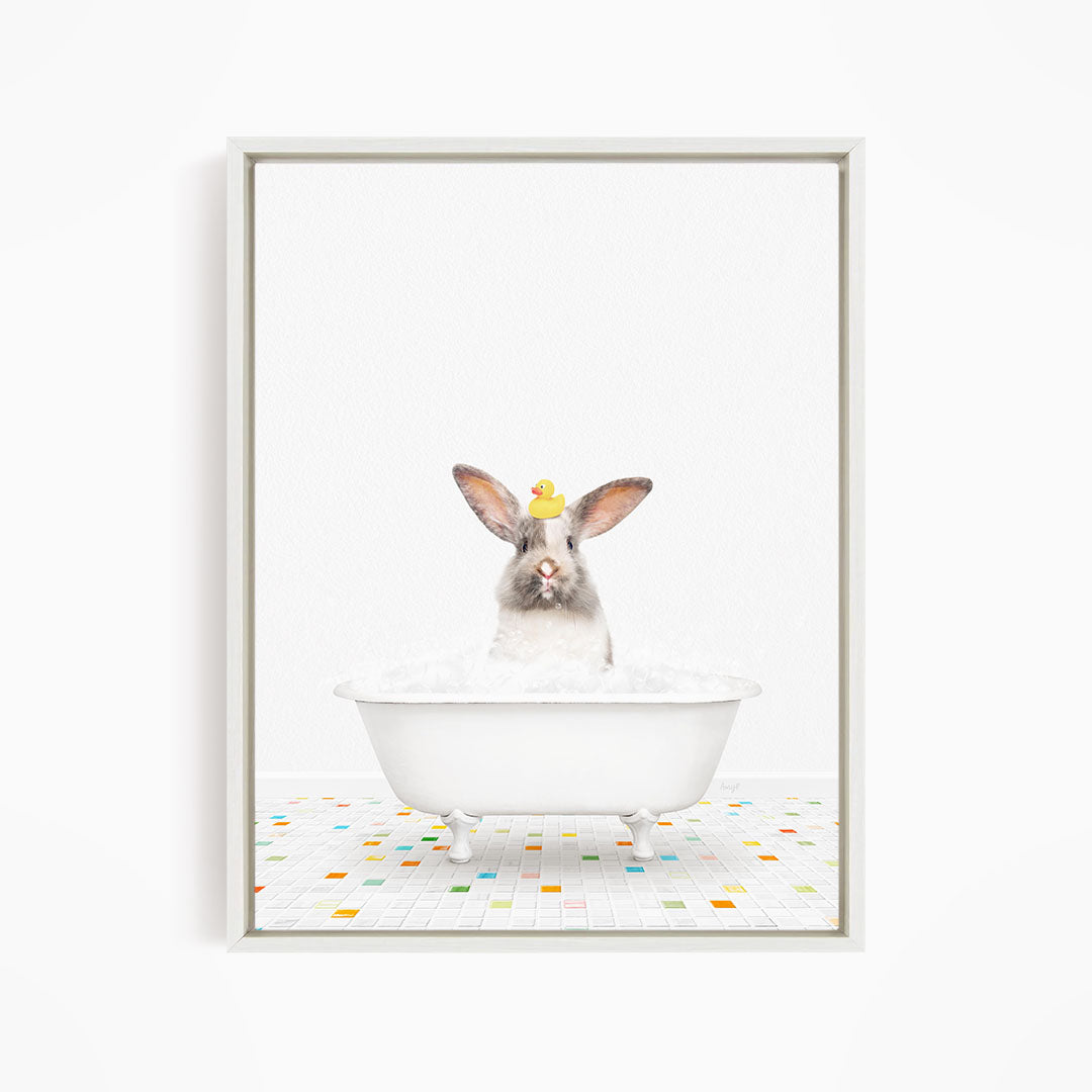 A white rabbit sitting in a white bathtub filled with bubbles, with a yellow rubber duck perched on its head.
