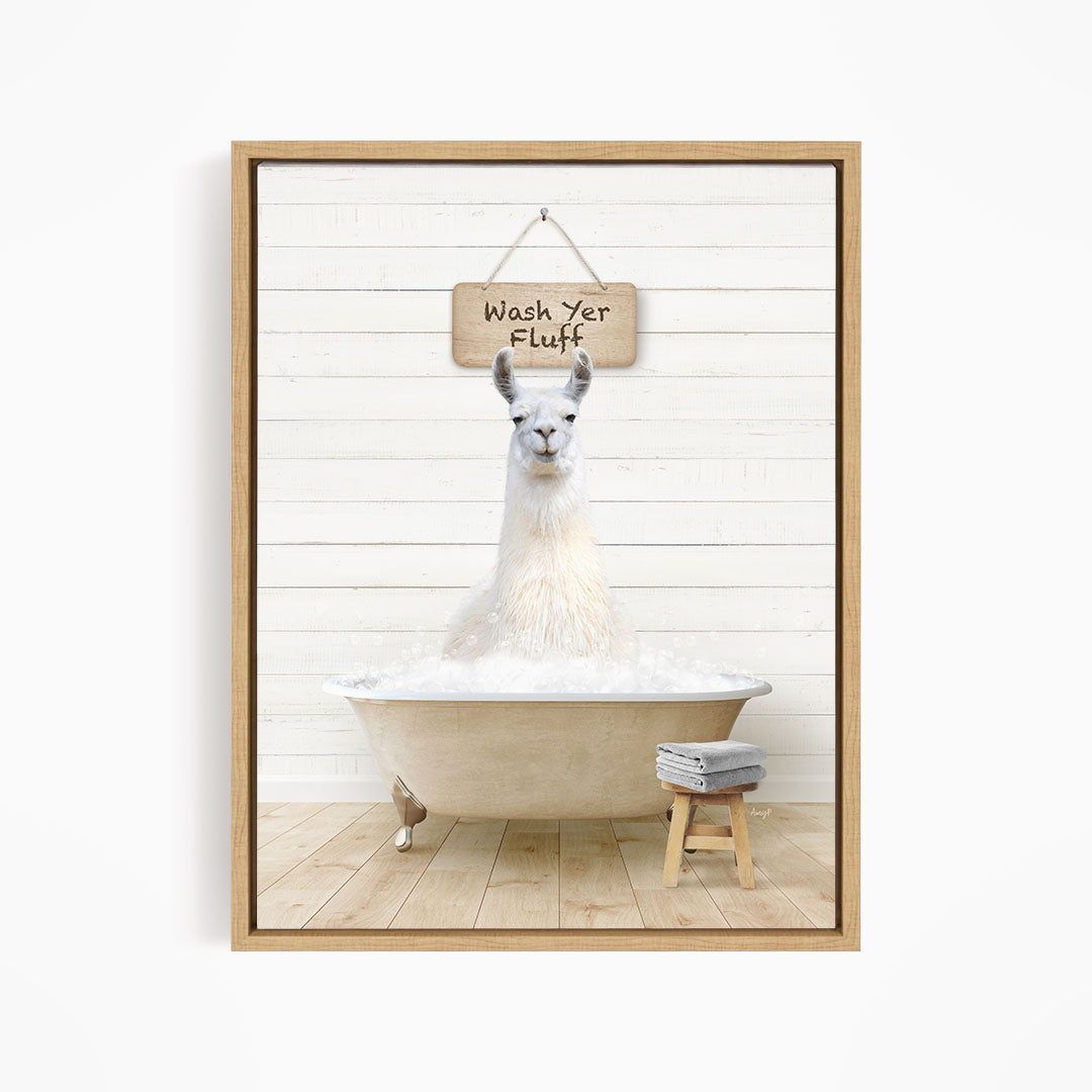 A white llama sitting in a bathtub filled with bubbles, with a wooden sign above it that says "Wash Yer Fluff".