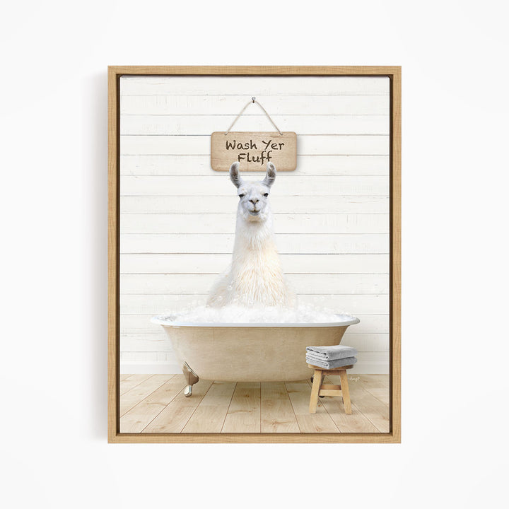 A white llama sitting in a bathtub filled with bubbles, with a wooden sign above it that says "Wash Yer Fluff".