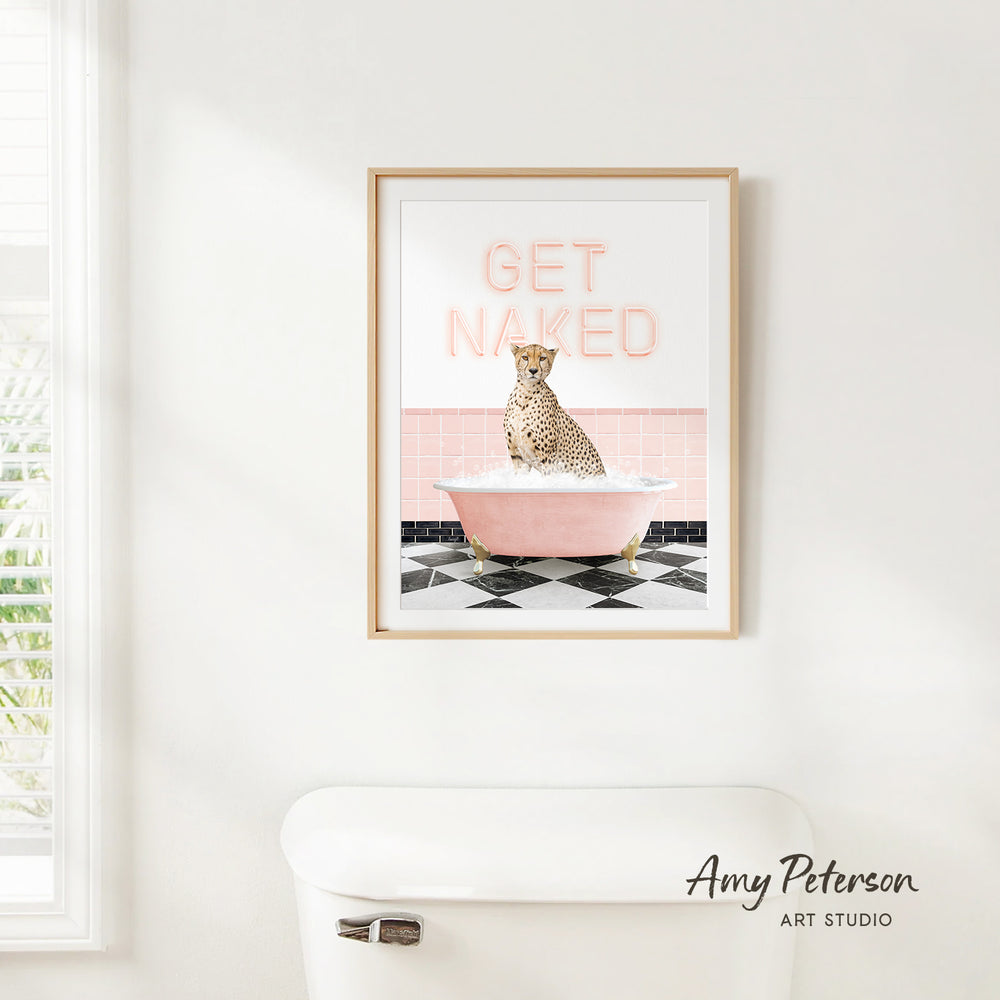 A framed print of a cheetah sitting in a pink bathtub with the text "GET NAKED" on it, hanging on a white wall.