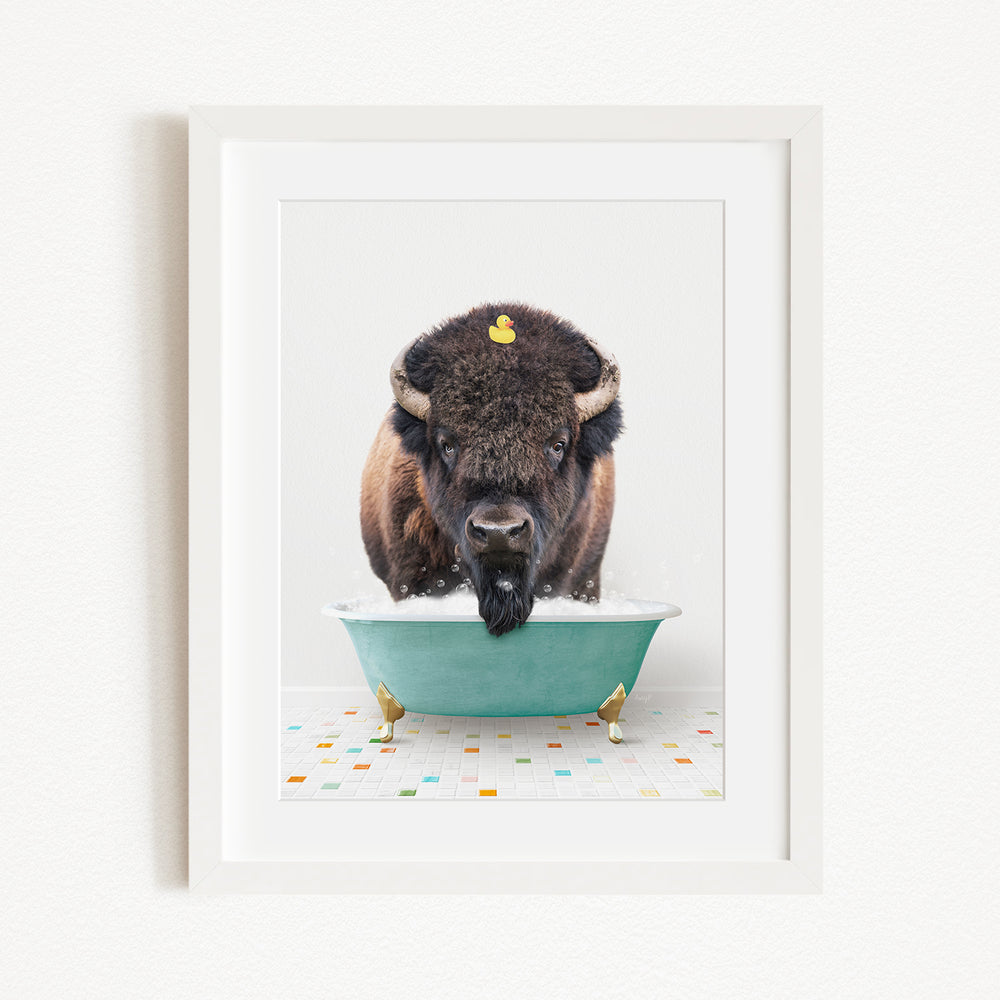 A buffalo with a yellow rubber duck perched on its head is sitting in a green bathtub, surrounded by colorful tiles on the floor.