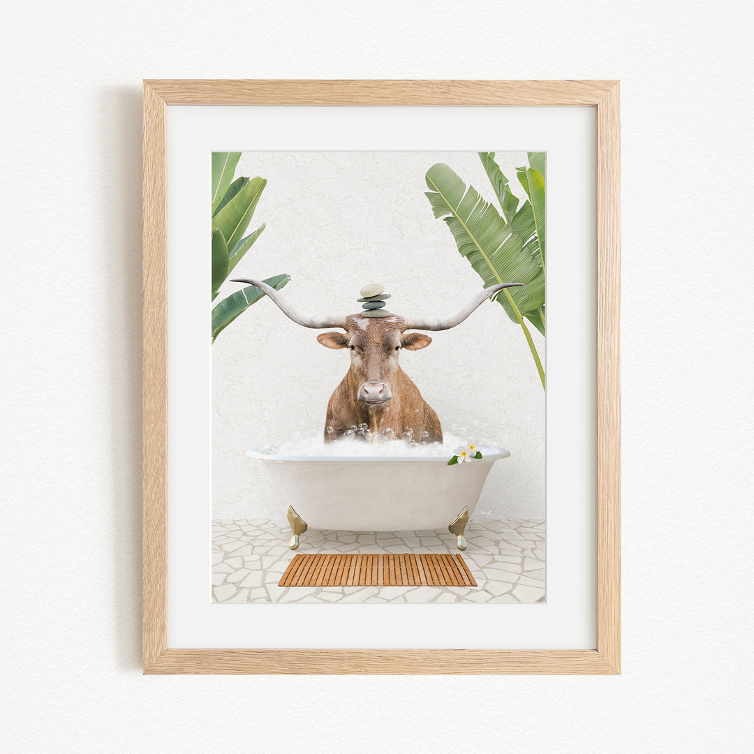 A framed image depicting a cow sitting in a bathtub filled with water, surrounded by tropical plants.