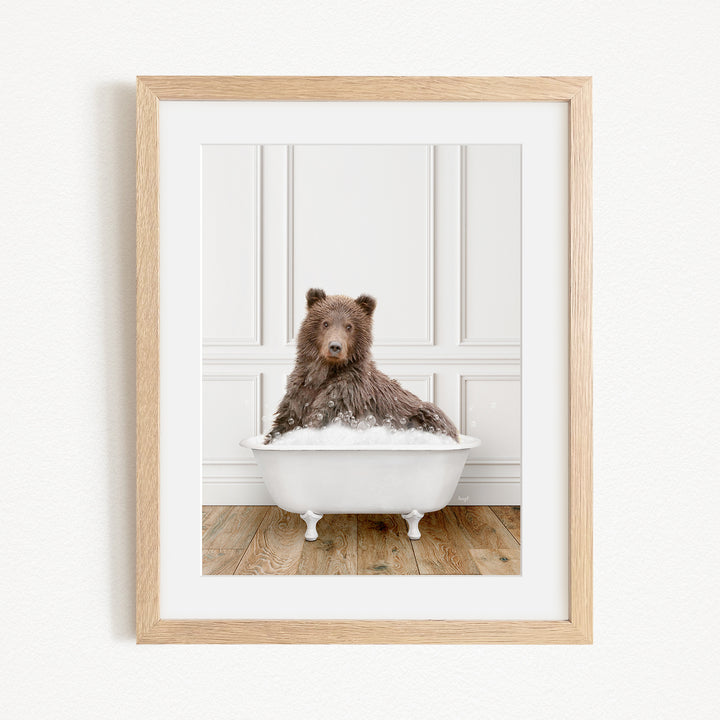 A brown bear sitting in a white bathtub filled with bubbles, looking directly at the camera.