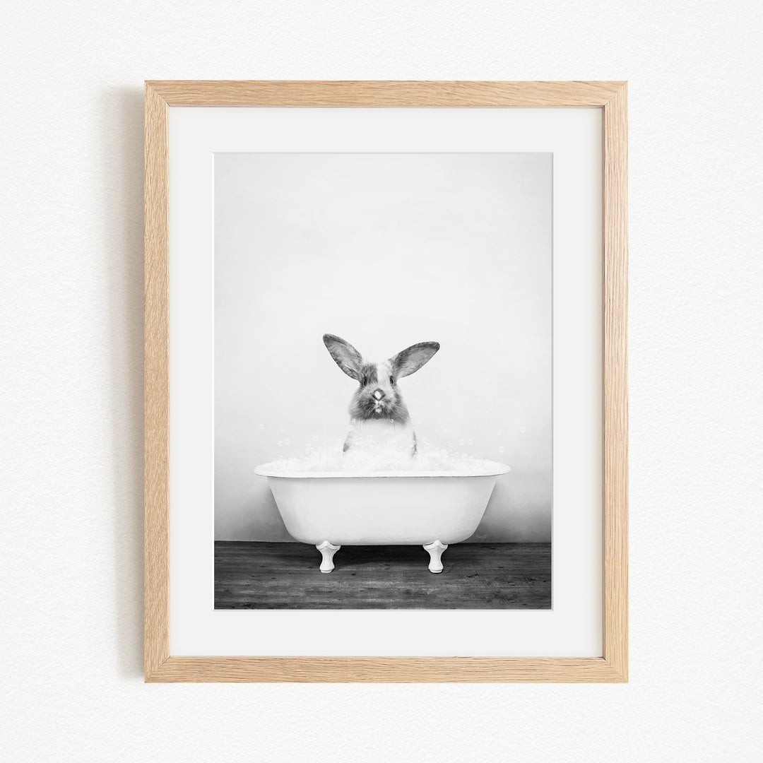 A black and white photograph of a rabbit sitting in a bathtub filled with water, looking directly at the camera.