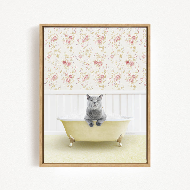 A gray cat sitting in a yellow bathtub filled with bubbles, with a floral wallpaper in the background.