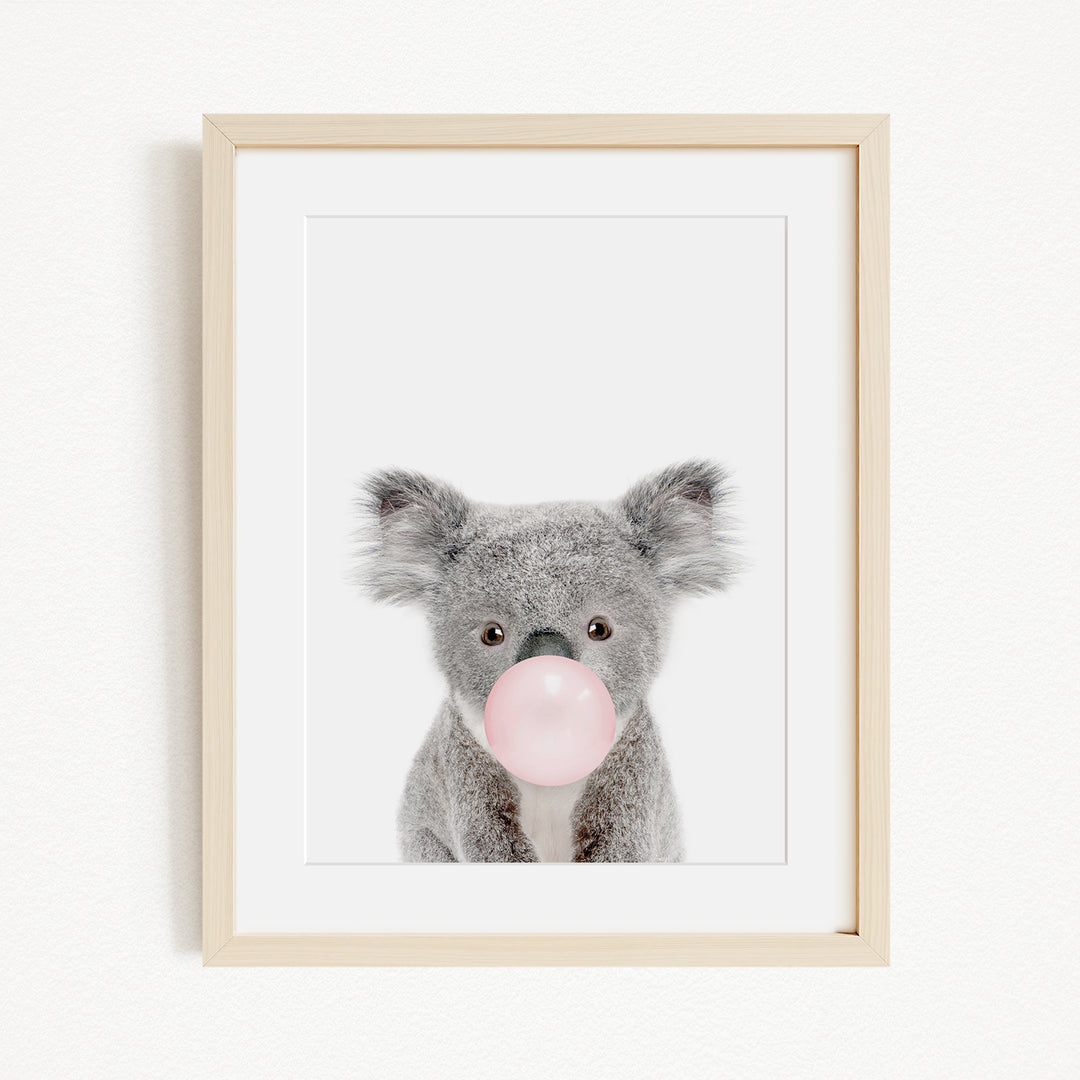 A framed image of a koala bear blowing a bubble with a pink bubblegum bubble.