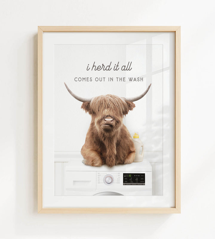 A framed image depicting a brown cow with horns sitting on a white washing machine, with the text "I herd it all comes out in the wash" above the cow.