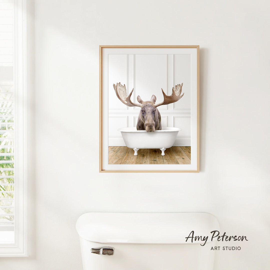 A framed image of a moose sitting in a bathtub, with its large antlers prominently displayed.