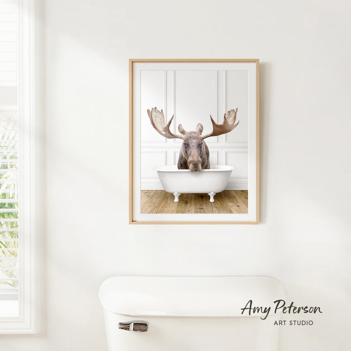 A framed image of a moose sitting in a bathtub, with its large antlers prominently displayed.