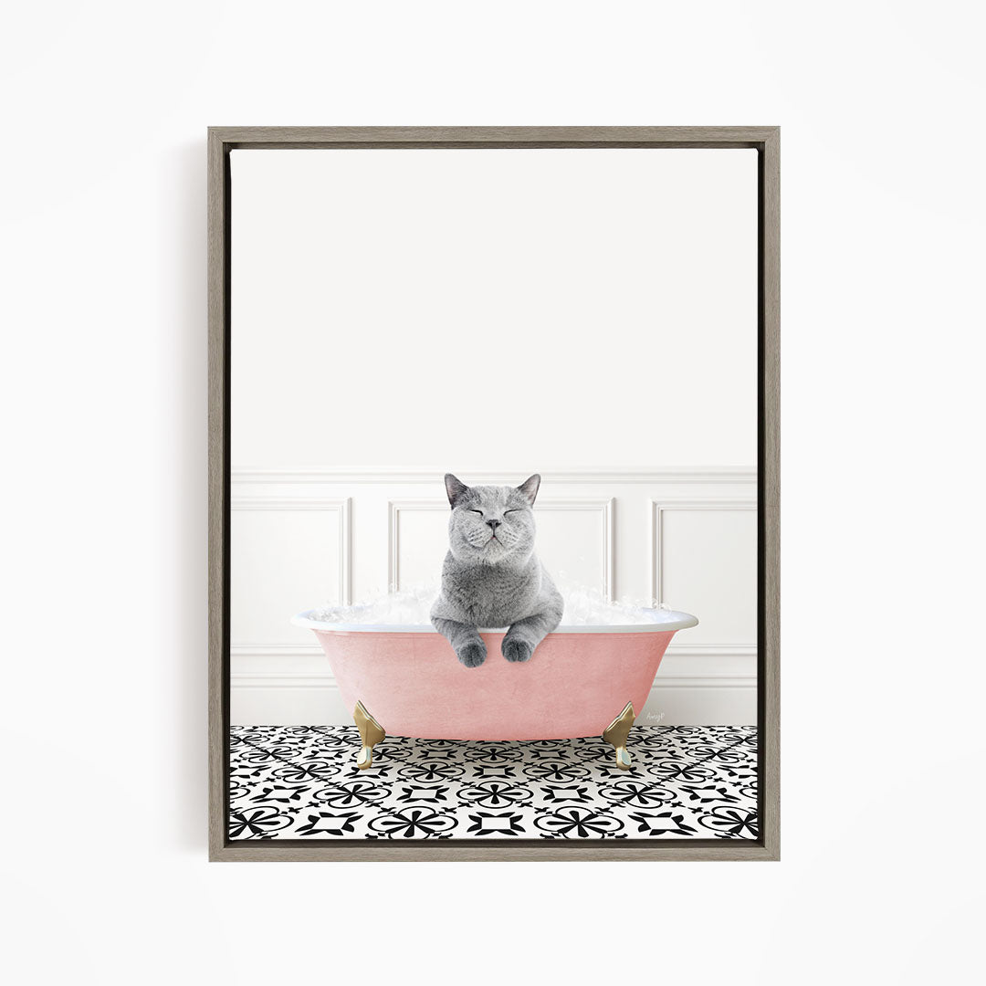 A gray cat sitting in a pink bathtub filled with bubbles, with a black and white patterned floor in the background.