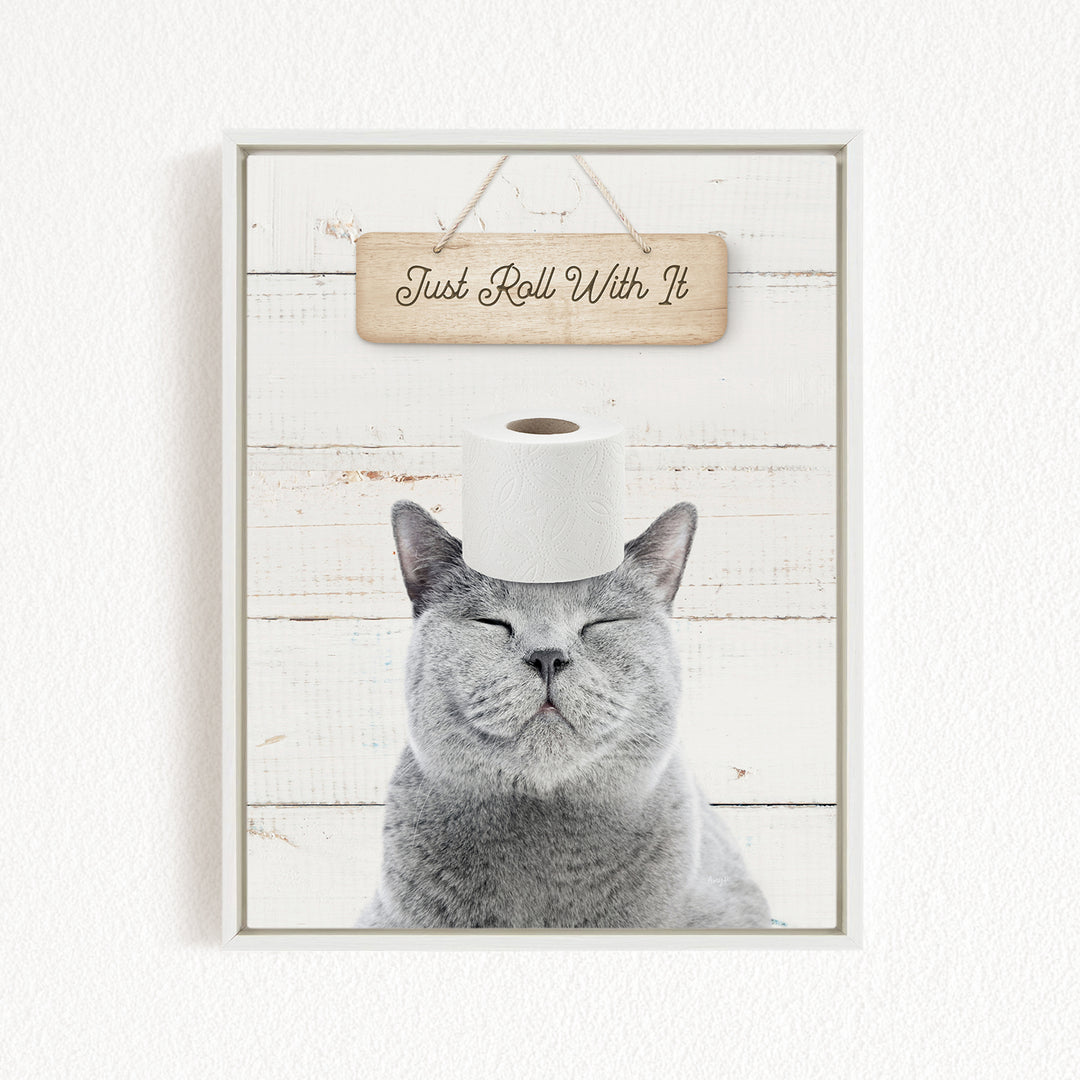 A gray cat with its eyes closed and a roll of toilet paper on its head, with a wooden sign above that says "Just Roll With It".