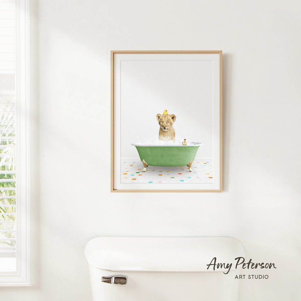 A framed print of a lion sitting in a green bathtub, surrounded by colorful tiles, is displayed on a white wall in a bathroom.