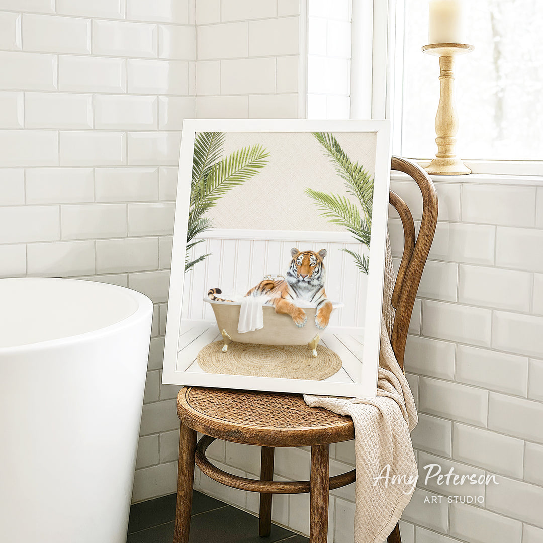 A framed image of a tiger sitting in a bathtub, surrounded by palm leaves, is displayed on a wooden chair in a bathroom setting.
