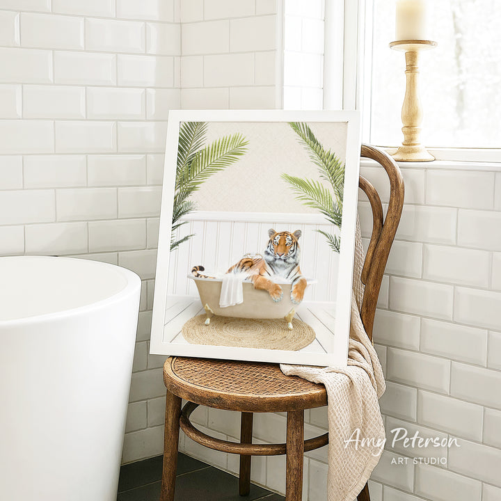 A framed image of a tiger sitting in a bathtub, surrounded by palm leaves, is displayed on a wooden chair in a bathroom setting.