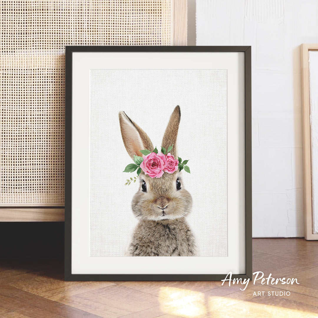 A framed print of a rabbit wearing a flower crown, with a white background and a wooden floor in the background.