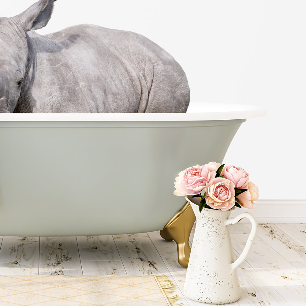 A gray rhinoceros is sitting in a green bathtub, with a vase of pink flowers placed next to it on a wooden floor.