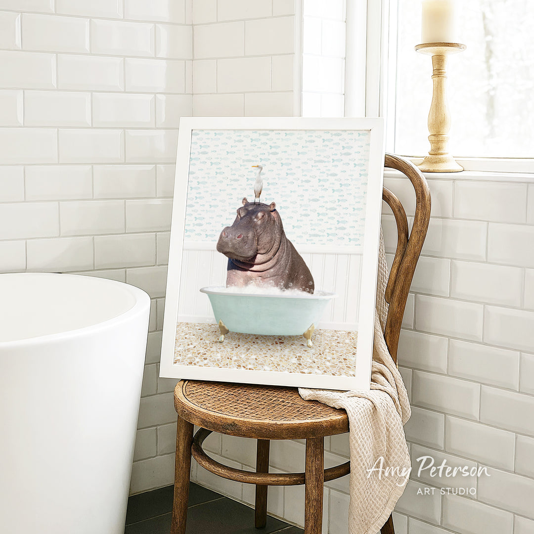 A framed image of a hippopotamus sitting in a bathtub, with a bird perched on its head, is displayed on a wooden chair in a bathroom setting.