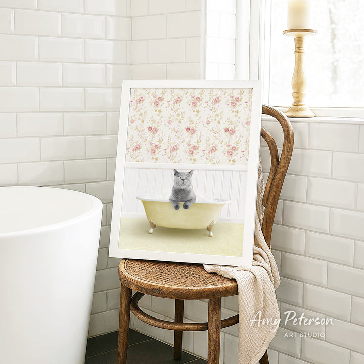 A framed image of a gray cat sitting in a yellow bathtub, with a floral pattern on the wall behind it.