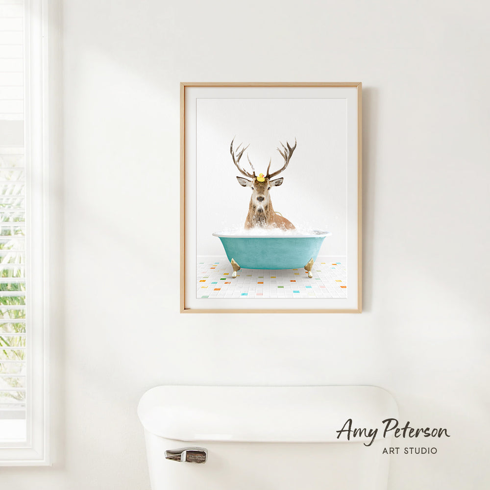 A framed image of a deer sitting in a blue bathtub, with a white toilet in the foreground.