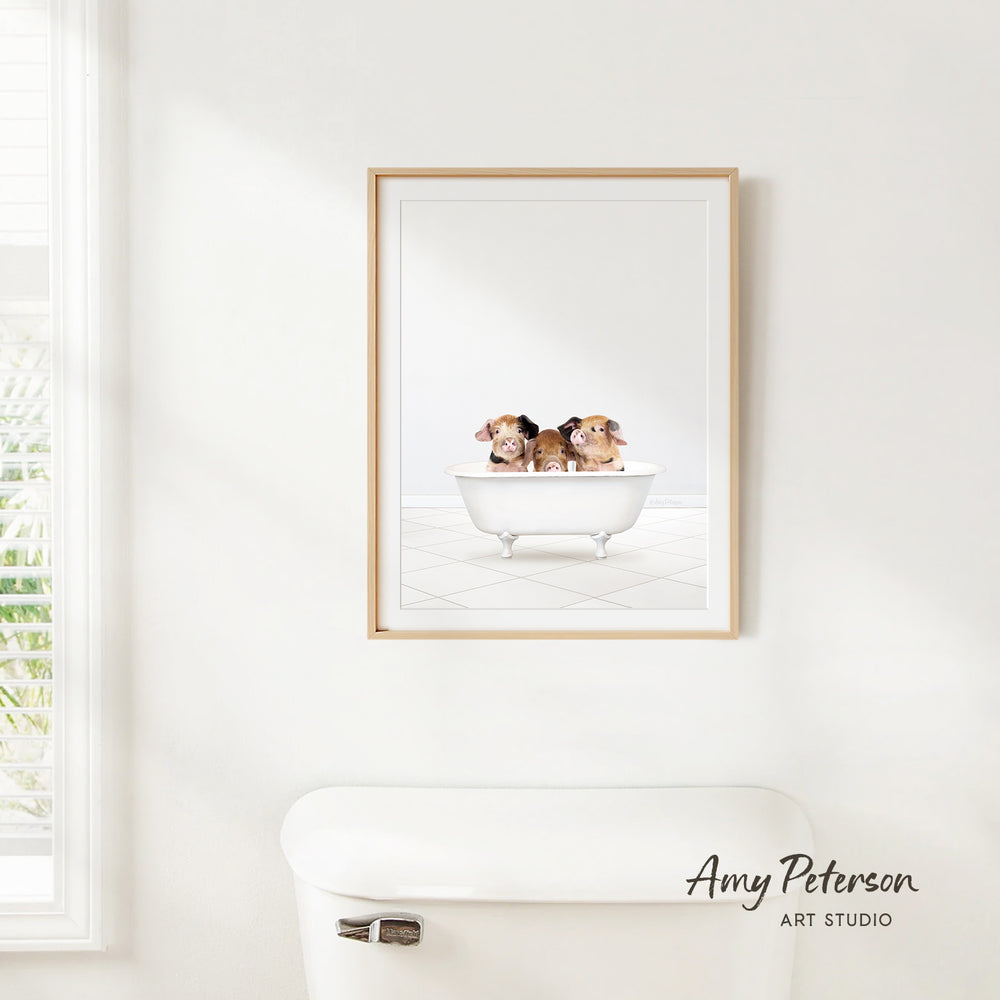 A framed image of two small brown dogs sitting in a white bathtub, with a window and a white toilet visible in the background.