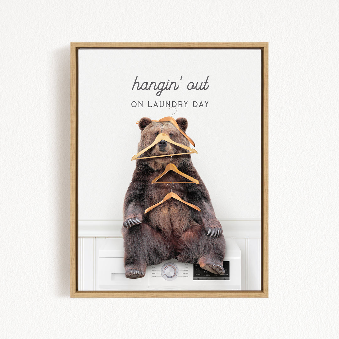 A framed image of a bear sitting on a washing machine, with a pile of clothes stacked on its head.