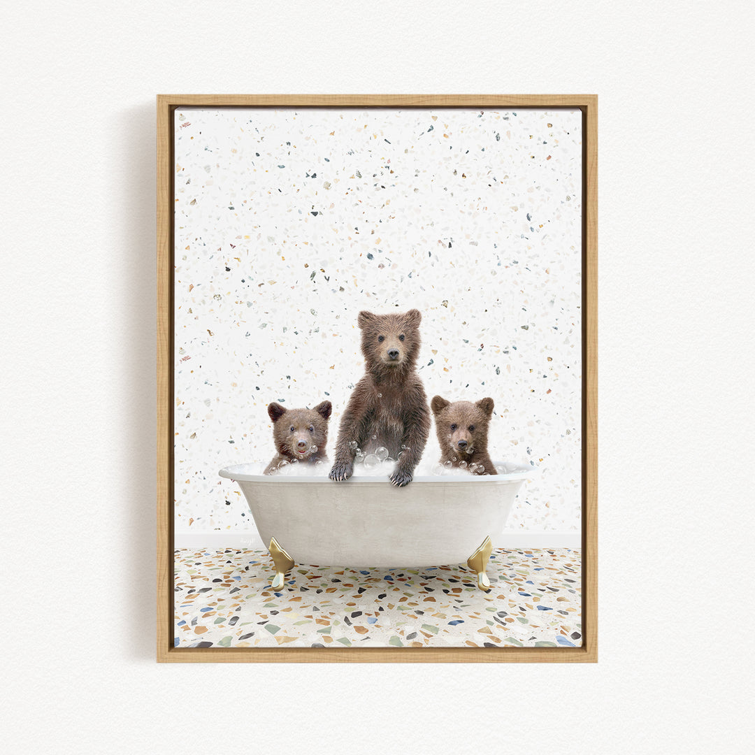 Three adorable brown bears sitting in a white bathtub, with a speckled tile floor beneath them.