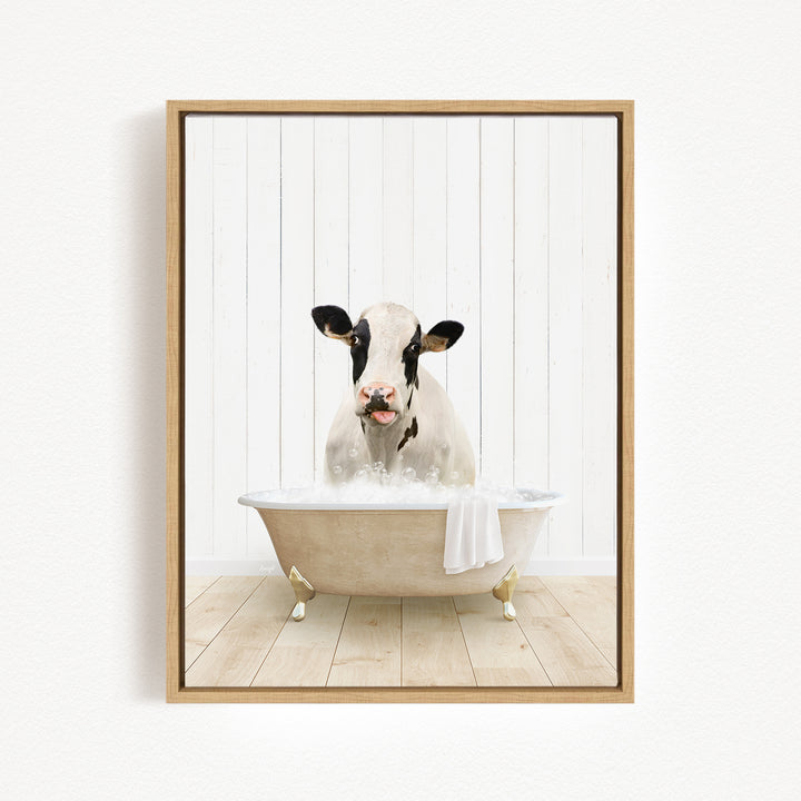 A black and white cow is sitting in a bathtub filled with water, with a towel hanging on the side of the tub.