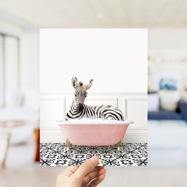 A zebra is sitting in a pink bathtub, surrounded by a black and white patterned floor.