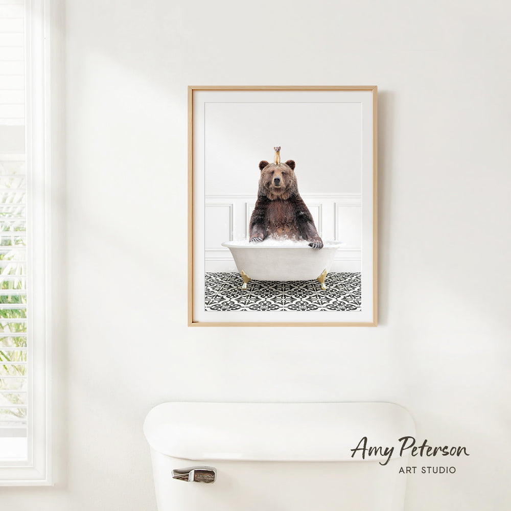 A framed image of a brown bear sitting in a white bathtub, with a patterned tile floor beneath it.