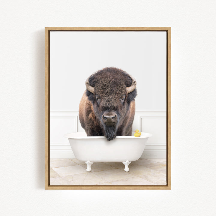 A buffalo with large horns is standing in a white bathtub, with a yellow rubber duck floating in the water.