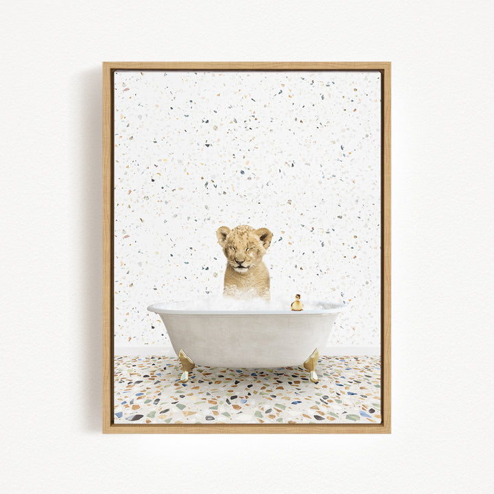 A young lion cub sitting in a white bathtub filled with water, surrounded by a speckled tiled floor.