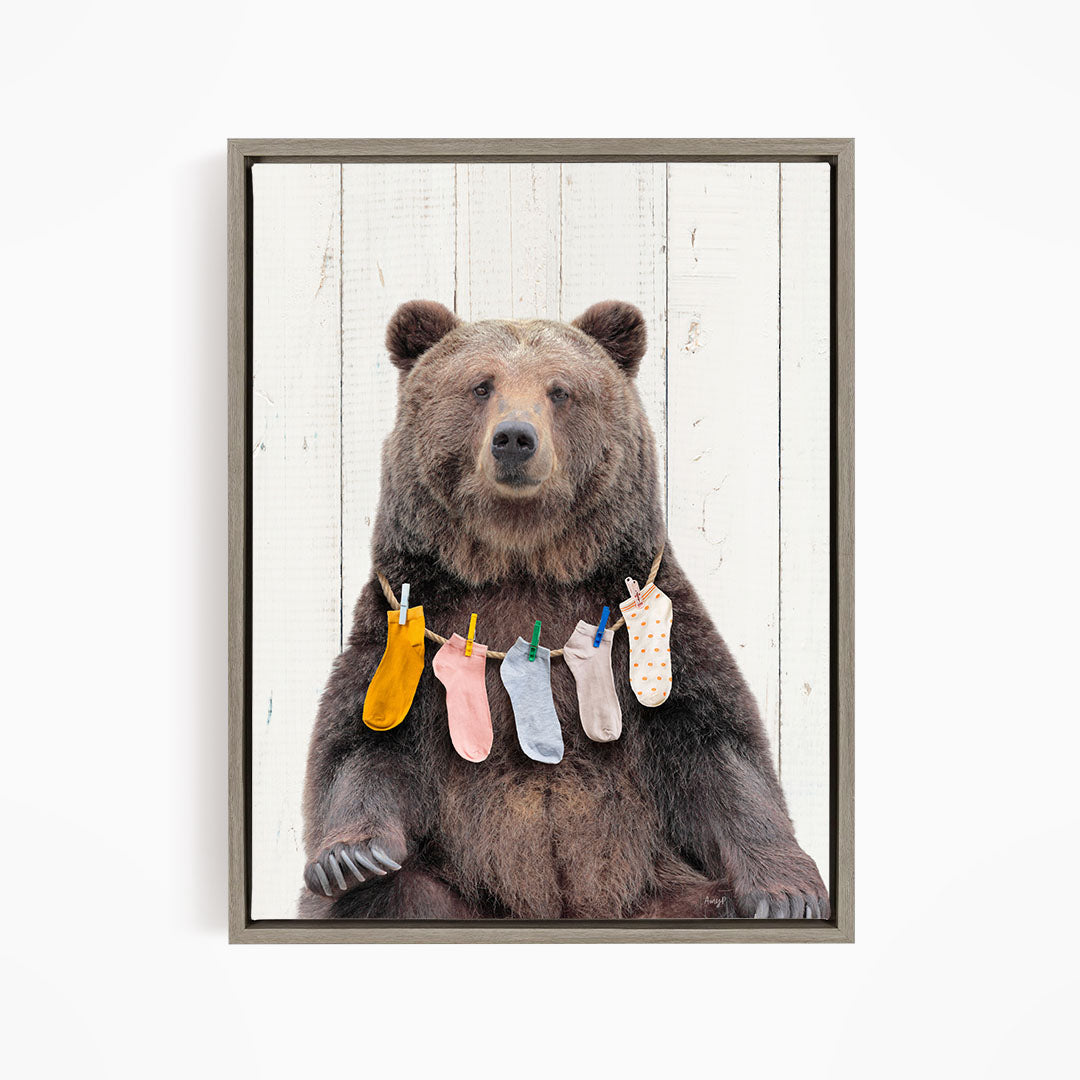 A large brown bear sitting on a wooden surface, wearing colorful socks hanging from a clothesline.
