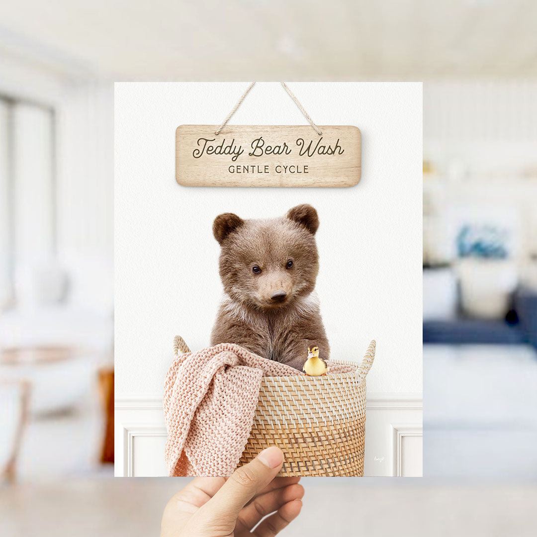 A wooden sign with the text "Teddy Bear Wash Gentle Cycle" hangs above a woven basket containing a teddy bear and a rubber duck.