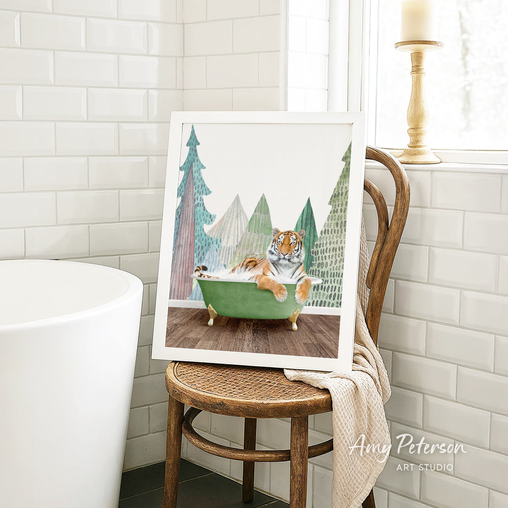 A framed painting of a tiger sitting in a green bathtub, surrounded by a snowy landscape with pine trees, is displayed on a wooden chair in a bathroom.