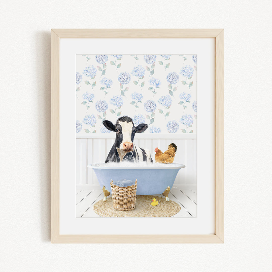 A framed image depicting a cow sitting in a bathtub, surrounded by a chicken and a duck, with a blue floral patterned wall in the background.