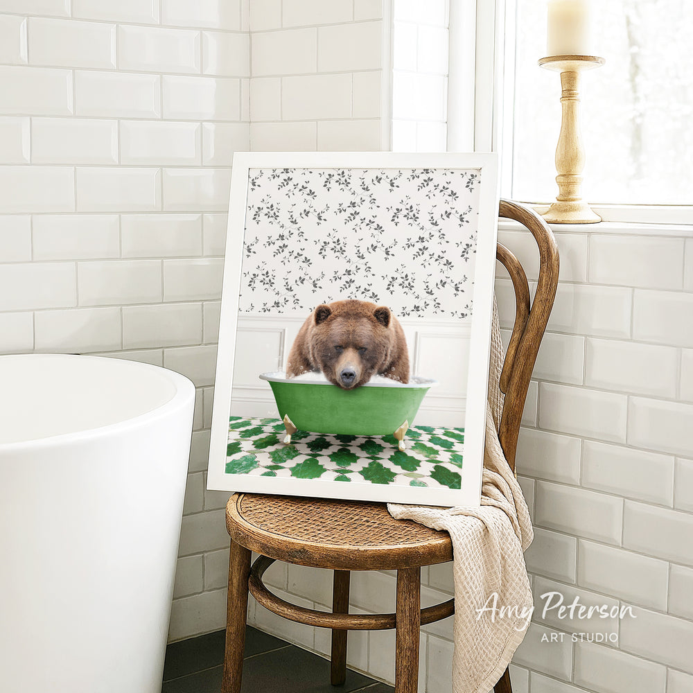 A framed image of a brown bear sitting in a green bathtub, with a floral pattern on the wall behind it.