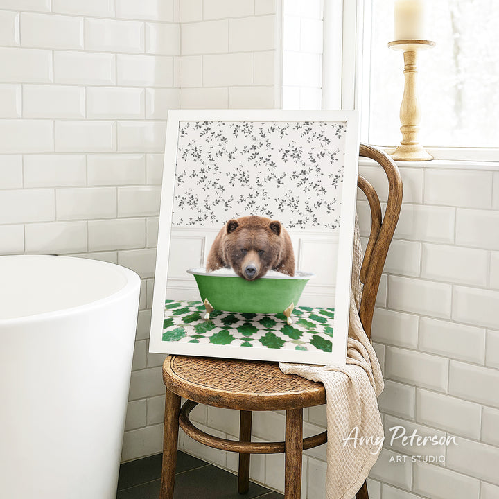 A framed image of a brown bear sitting in a green bathtub, with a floral pattern on the wall behind it.