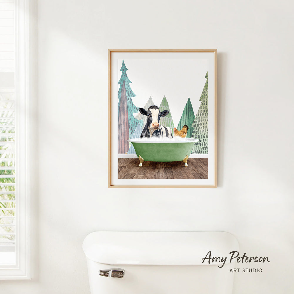 A framed print of a cow sitting in a green bathtub, surrounded by trees, is hanging on a white wall.