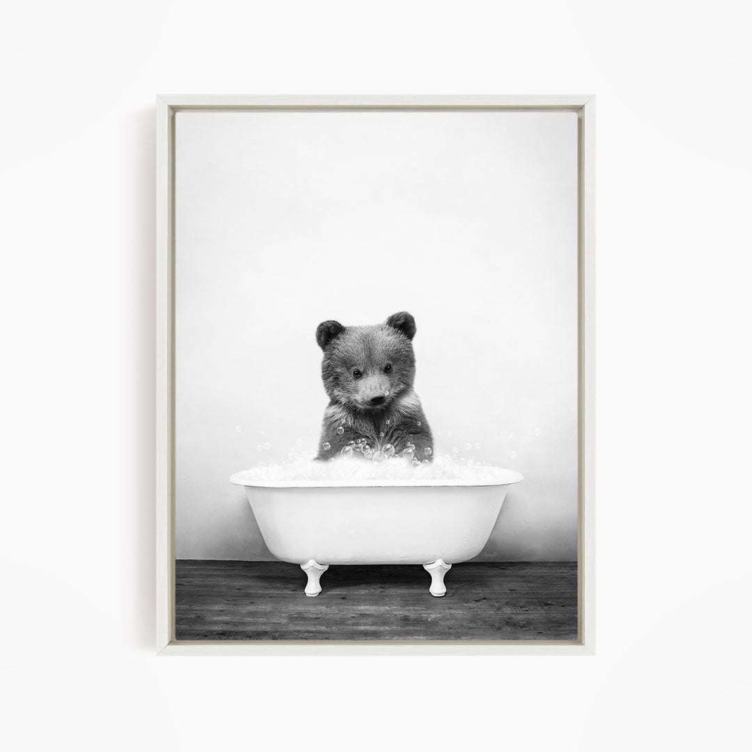 A black and white image of a bear sitting in a bathtub filled with water.