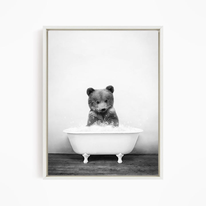 A black and white image of a bear sitting in a bathtub filled with water.