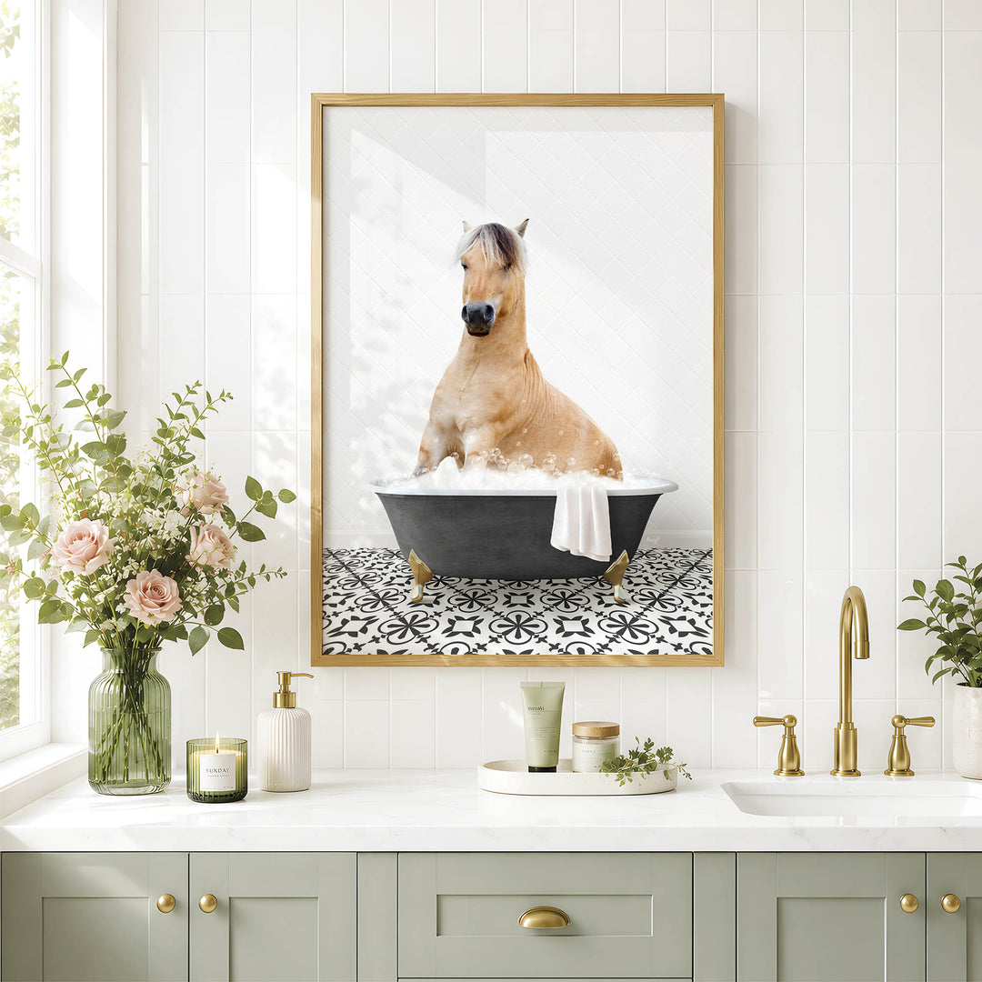 A framed image of a horse sitting in a bathtub, surrounded by flowers and a decorative vase, is displayed on a white tiled wall above a bathroom sink.