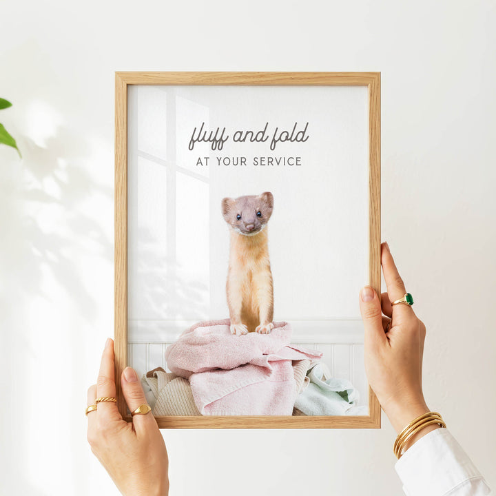 A person's hands holding a framed picture of a small animal, likely a cat, sitting on a pile of clothes.