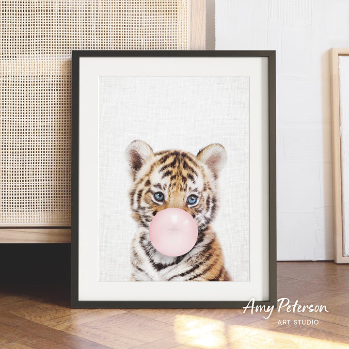 A framed photograph of a young tiger cub blowing a bubble with a pink bubble gum bubble.