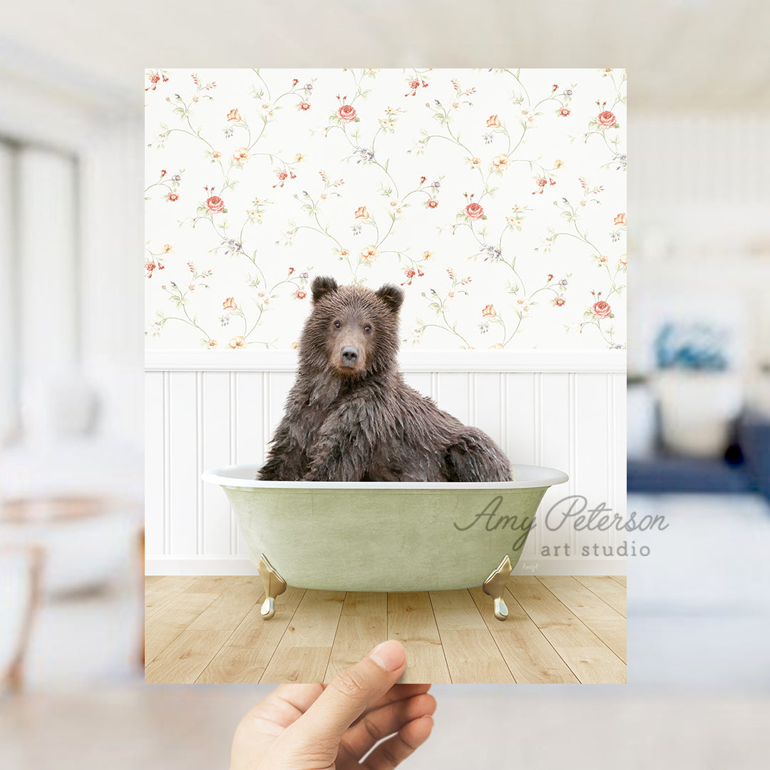 a hand holding up a photo of a bear in a bathtub