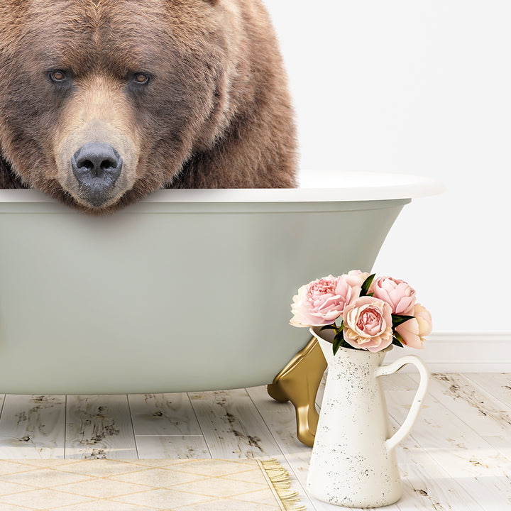 A large brown bear is sitting in a white bathtub filled with water, with a vase of pink flowers placed next to it on the floor.