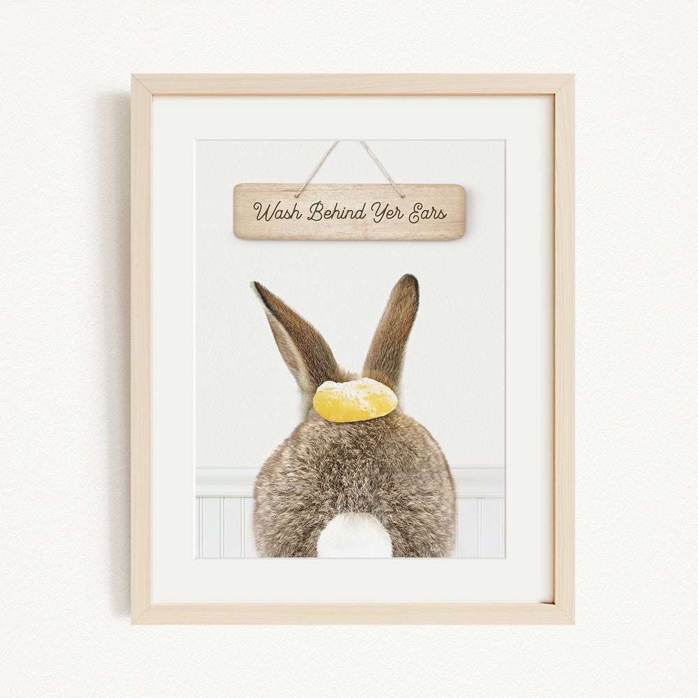 A framed image of a rabbit with a sign that says "Wash Behind Yer Ears" hanging above it.
